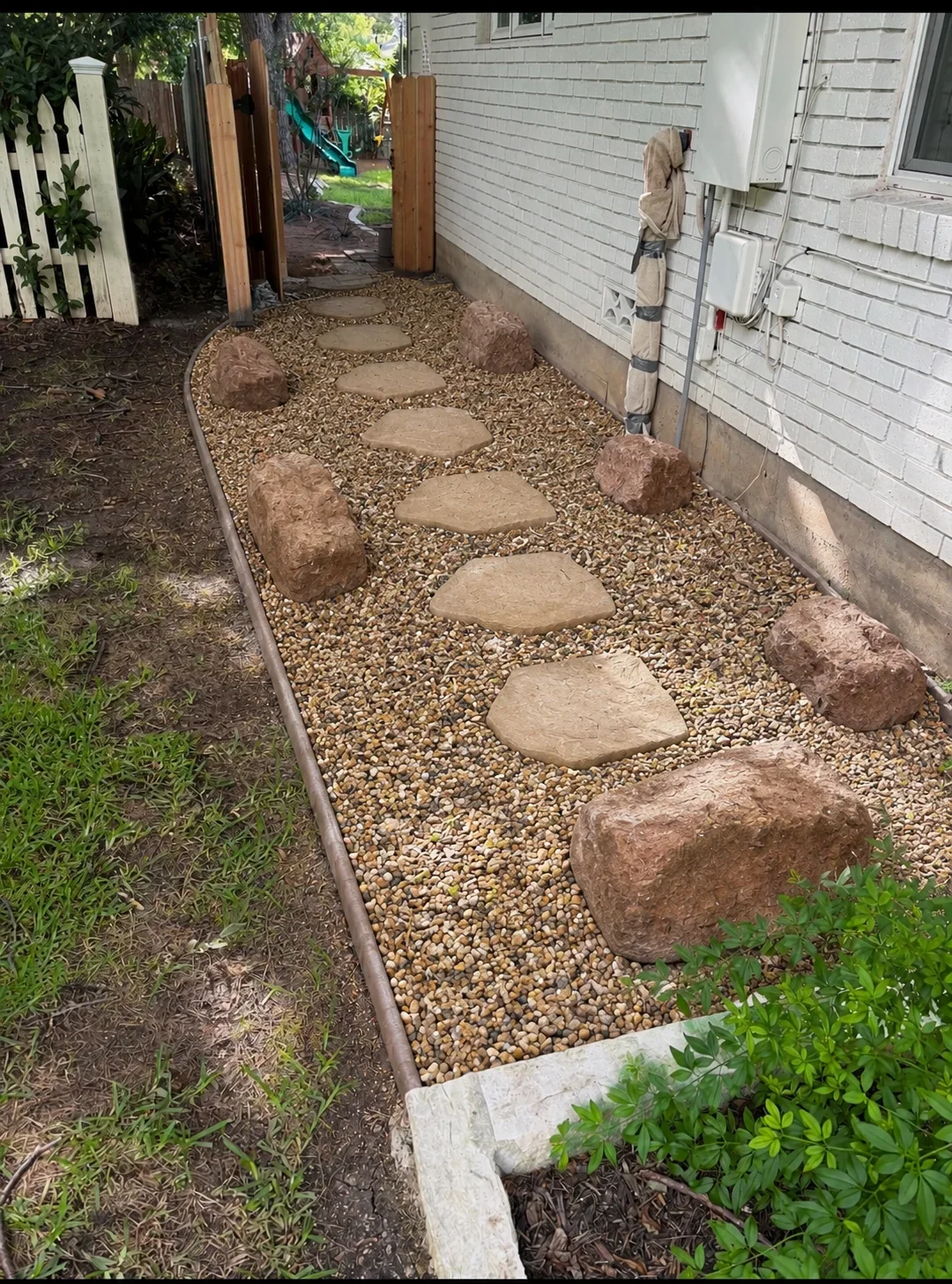 Gravel walkway with stepping stones and boulders along house foundation